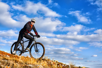Naklejka premium Cyclist riding his bike down on mountain trail. Beautiful sky and clouds on background