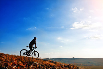 Fototapeta na wymiar Cyclist riding his bike down on mountain trail. Beautiful sky and clouds on background