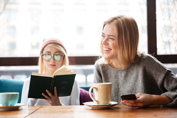 Young women friends reading book and drinking coffee.
