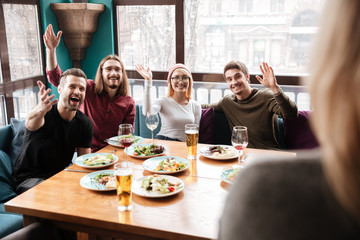 Happy friends sitting in cafe while waving