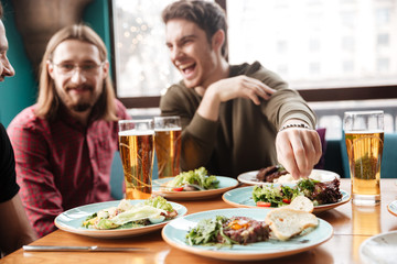 Young cheerful friends sitting in cafe while drinking alcohol.