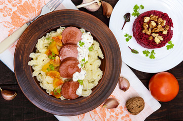 Galetti Pasta with pieces of sausage, yellow tomatoes and creamy mustard sauce in a clay bowl and beet salad with nuts on dark wooden background. The top view