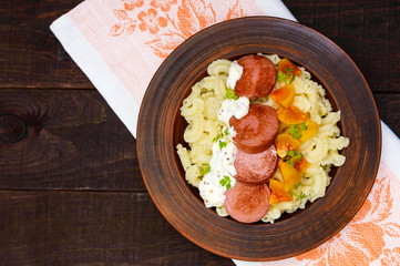 Galetti Pasta with pieces of sausage, yellow tomatoes and creamy mustard sauce in a clay bowl on dark wooden background. The top view