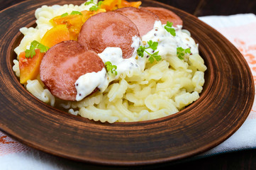 Galetti Pasta with pieces of sausage, yellow tomatoes and creamy mustard sauce in a clay bowl on dark wooden background.