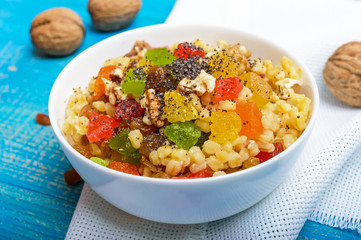 Diet fitness wheat porridge with nuts, raisins, slices of citrus fruit (grapefruit, orange, kiwi), poppy seeds, honey, in a white bowl on a blue wooden background.