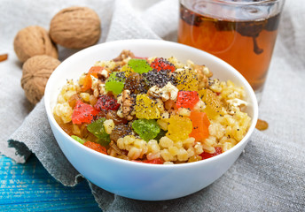 Diet fitness wheat porridge with nuts, raisins, slices of citrus fruit (grapefruit, orange, kiwi), poppy seeds, honey, in a white bowl on a blue wooden background.