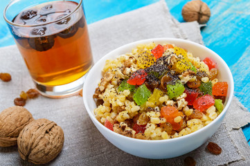Diet fitness wheat porridge with nuts, raisins, slices of citrus fruit (grapefruit, orange, kiwi), poppy seeds, honey, in a white bowl on a blue wooden background.