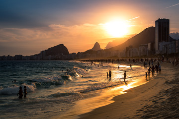 Blick auf den Sonnenuntergang am Strand der Copacabana mit Bergen im Horizont und hohem Hotelgebäude, Rio de Janeiro