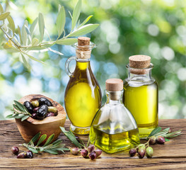 Olive oil and berries are on the wooden table under the olive tree.