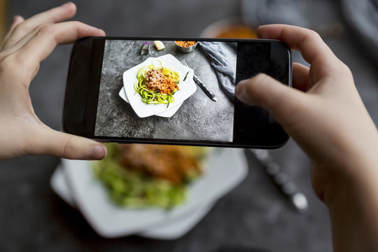 Girl taking a photo zoodles with vegetarian Bolognese sauce with her smartphone, close-up