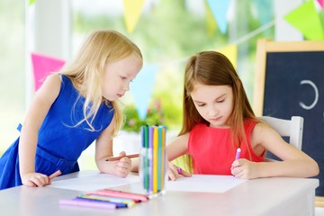 Two cute little sisters drawing with colorful pencils at a daycare