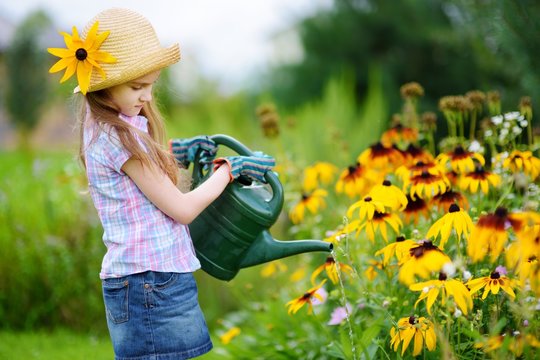 Cute Little Girl Watering Flowers In The Garden