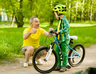 Naklejka premium Grandfather talking with his grandson riding a bicycle