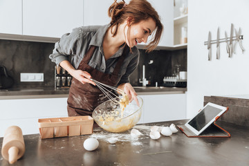 Cheerful woman cooking and looking at tablet computer.