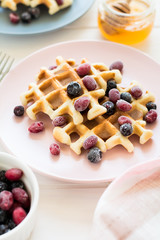 Belgian waffles with honey and frozen berries on white wooden table. Selective focus