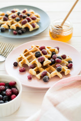 Belgian waffles with honey and frozen berries on white wooden table. Selective focus