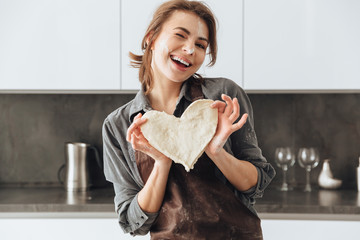 Cheerful lady holding the dough heart.