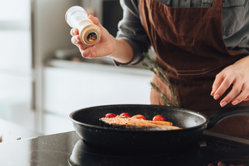 Cropped image of young attractive woman cooking fish