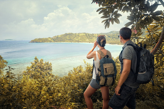 Couple hikers with backpacks watching through binoculars enjoying view coast.