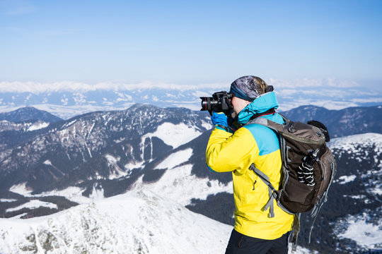adventure outdoor photographer with backpack and tripod shooting pictures in winter high mountains