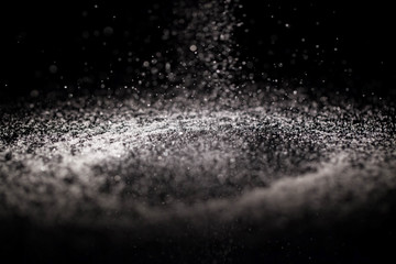 Crystals of sugar fall on black glass table