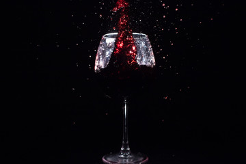 Red juice splashes in a crystal glass standing in black space