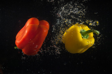 Red and yellow peppers fall in water on black background