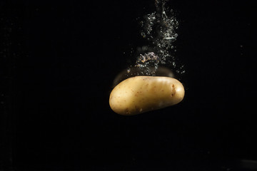 Delicious raw potato sinks in water on black background