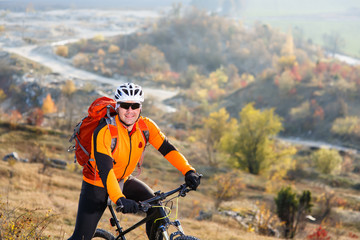 Man in helmet and glasses, with backpack stay on the bicycle under landscape with rocks and hill.