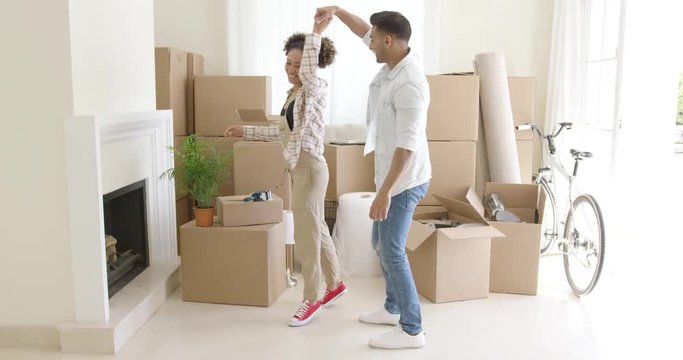 Adorable and happy mixed race couple  dancing in the living room of their new home just after moving in. They are surrounded by unpacked boxes.