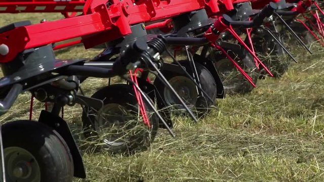 We can see fast movements of rotary rakes. The tractor is pulling a trailor very slowly behind it, the wheels are moving slowl.
