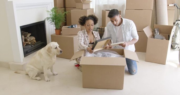 Young woman petting her pet dog as it sits calmly watching her and her husband pack their belongings ready to move house