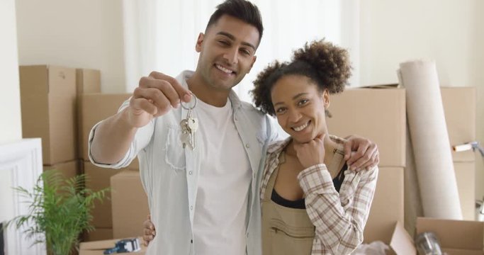 Proud young African American couple with keys to anew home standing arm in arm in front of a stack of packing boxes smiling