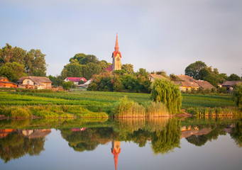 Fototapeta na wymiar Magnificent landscape. Village Roman Catholic Church on the lake in summer. 