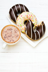 Cup of coffee and tasty donuts with icing and chocolate on white wooden background, copy space