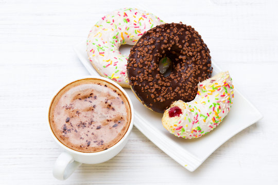 Cup of coffee and tasty donuts with icing and chocolate on white wooden background, copy space