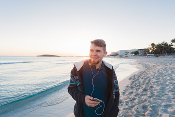 Happy man walking on the beach while listening music with earphones.