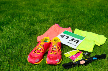 Running shoes, marathon race bib (number), runners gear and energy gels on grass background, sport, fitness and healthy lifestyle concept
