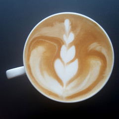 Top view of a mug of latte art coffee on black background.