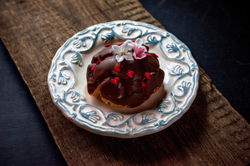 Eclair dark chocolate glaze, with decor red hearts and grapes on a dark wooden background, on a ceramic plate.
