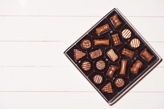 top view of various chocolate pralines in box on white wooden background.