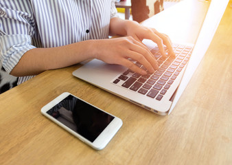 Woman office worker is typing keyboard of laptop with mobile phone, business or learning concept