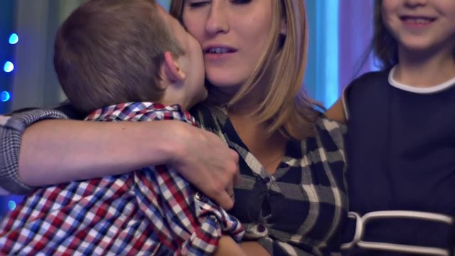 Happy Mom Hugs Kisses His Son and Daughter Tenderly Family Celebrates Christmas Holidays at Home Pregnant Mom and Two Her Children Roses Made of Fabric