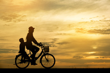 Fototapeta na wymiar Silhouette of mother and child,cycling togetherThe background image is a sunset in Thailand