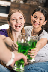 Happy young women clinking glasses with green beer while celebrating St Patricks Day