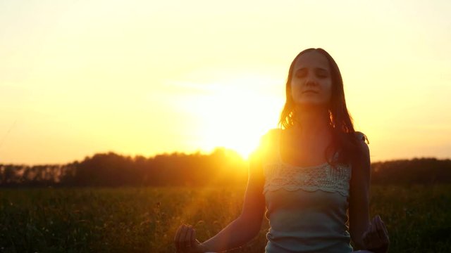 Young beautiful brunette woman meditates in the field during amazing sunset with sun flare effects. 3840x2160
