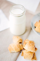 Home made croussants over fabric material with milk in bottle.