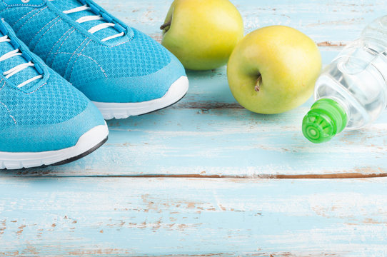 Sport shoes, apples, bottle of water on blue wooden background. Concept healthy lifestyle, healthy food, sport and diet. Sport equipment