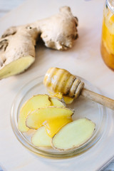 Slices of ginger with spoon of honey on glass plate.