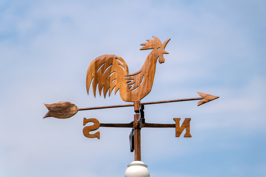 Wooden rooster weathervane showing a wind direction. Traditional weathercock on heaven background. Decorative cock weathervane close up.